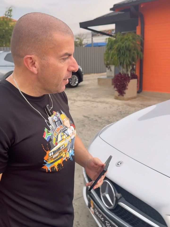 Uncle Bobby with his phone next to a white Mercedes at the dealership